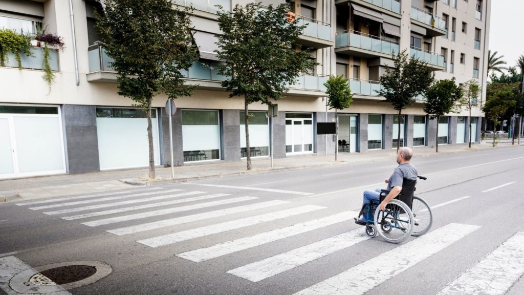 PMR en fauteuil roulant traversant la route sur un passage piétons. Norme trottoir pmr