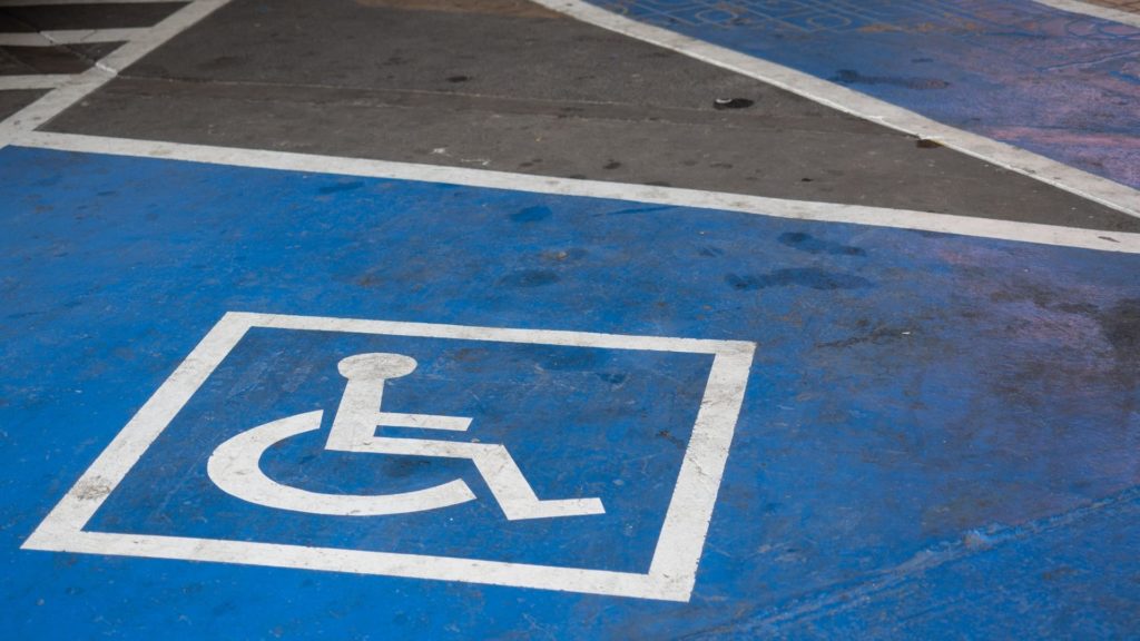 Dessin bleu et blanc pour une place de stationnement handicapé. Fond bleu avec dessin d'une personne en fauteuil roulant blanc dans un carré.
